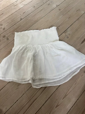 Vit kortkjol med smock i midjan - Söt vit kortkjol med bred smock i midjan och lätt utställd, luftig kjoldel. Kjolen är gjord i ett tunt, mjukt tyg som känns perfekt för varma dagar. Enkel och stilren design som passar till det mesta. Skriv för fler bilder😊