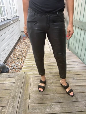 Svarta fuskskinnbyxor med dragkedjor - Snygga svarta byxor i fuskskinn med tight passform och dragkedjor framtill. Baksidan har quiltade detaljer upptill och stretchigt tyg för extra komfort. Perfekta för dig som vill ha en edgy look.