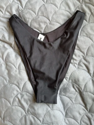 Svart stringtrosa från BikBok - Säljer en svart stringtrosa från BikBok med hög midja och slät, stretchig yta. Trosan har en enkel och stilren design utan spets eller dekorationer, perfekt för dig som gillar minimalistiskt underklädesmode.
