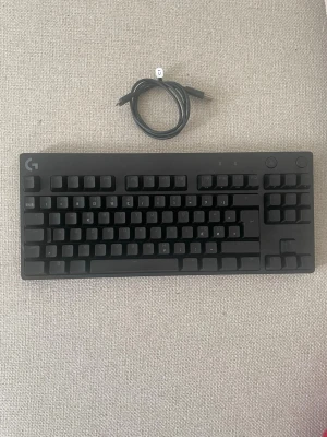 Logitech G Pro mekaniskt tangentbord - Säljer ett svart Logitech G Pro mekaniskt tangentbord med RGB-belysning. Kompakt design utan numerisk del, perfekt för gaming eller skrivbordet. Tangentbordet har avtagbar USB-kabel och robust plastkonstruktion. Snyggt och stilrent med programmerbar belysning.