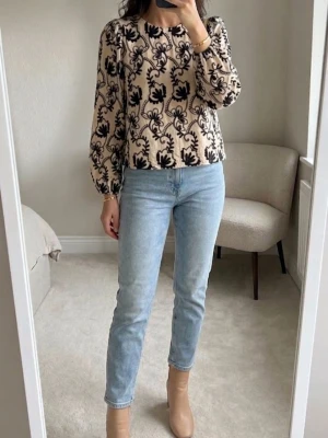 Beige blommig blus från Object - Trendig beige blus från Object med svart blommigt mönster. Modellen har rund halsringning, puffiga långärmar och en rak passform. Materialet känns mjukt och lätt, perfekt för dig som gillar en unik och stilren look.