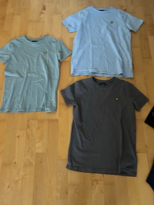 3-pack Lyle & Scott t-shirts - Säljer tre klassiska t-shirts från Lyle & Scott i ljusblått, ljusgrönt och mörkgrått. Alla har rund hals, korta ärmar och den ikoniska gula loggan på bröstet. Perfekta basplagg i mjuk bomull som funkar till allt. Säljer alla tre i ett paket. Pris kan diskuteras!