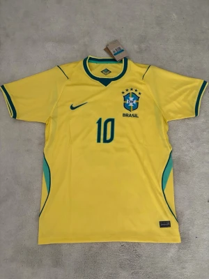 Brasilien Nike fotbollströja gul M - Gul Brasilien fotbollströja från Nike med gröna detaljer, nummer 10 på bröstet och CBF-emblem. Tröjan har korta ärmar, rund hals med grön kant och är tillverkad i ett lätt, ventilerande material perfekt för träning eller match.
