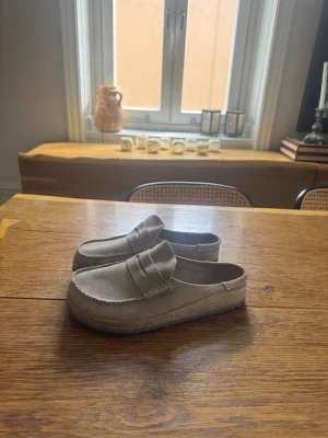 Birkenstock Naples beige  - Stilrena beige slip-in sandaler i mjuk mocka med klassisk penny strap och rundad tå. Skorna har en låg, bekväm gummisula och enkel design som ger en avslappnad vibe. Perfekta för dig som gillar minimalistisk stil. Typ helt nya, har använt dom väldigt få gånger. 
