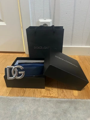Blått skärp från Dolce & Gabbana - Snyggt blått skärp från Dolce & Gabbana med stor DG-logga i silver som spänne. Skärpet är gjort i skinn och har en stilren design som passar till många olika outfits. Kommer i originalask och påse.