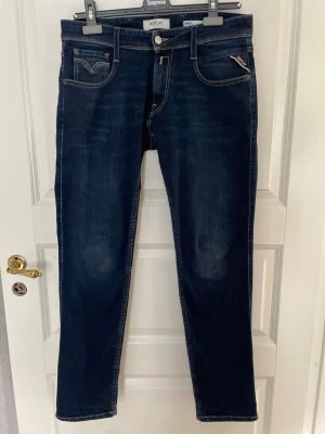  Replay Anbass - Snygga mörkblå jeans från Replay med raka ben och klassiska kontrastsömmar. Jeansen har fem fickor, silverfärgade detaljer och en liten logotyp på bakfickan. Materialet är mjukt denim som sitter skönt och passar till många olika stilar.