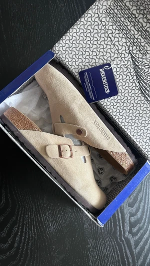 Beige Birkenstock Boston tofflor - Säljer ett par beige Birkenstock Boston tofflor i mocka. De är i helt nytt skick och box ingår. Storlek 42