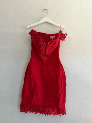 Röd spetsklänning från Ax Paris - Snygg röd kortklänning från Nelly  med v-ringning och spetsdetaljer längs urringning och fåll. Klänningen har offshoulder-band och figurnära passform.