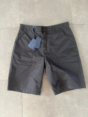 Svarta shorts från Prada i nylon - Snygga svarta shorts från Prada. Nytt skick med lapp kvar. Perfekta till sommaren. Storlek 33, passar någon mellan M/L