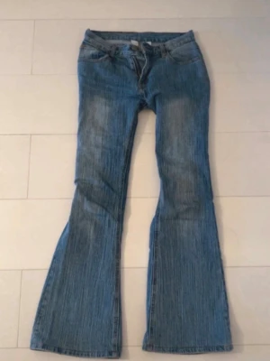 Blå utsvängda jeans med hög midja y2k - Säljer ett par blå jeans med utsvängda ben och hög midja. Klassisk femficksmodell med dragkedja och knapp framtill. Jeansen har en snygg tvättad look och är tillverkade i denim. Perfekta för en trendig och avslappnad stil.