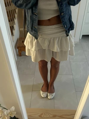 Vit volangkjol - Söt vit kortkjol med dubbla volanger och lätt struktur i tyget. Kjolen har en bred midjeresår och är perfekt för en fräsch och somrig look. Passar till både sneakers och ballerinas för en avslappnad stil. Från gina, storlek 36!