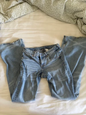Ljusblå bootcut low waist jeans från H&M - Säljer ett par ljusblå bootcut low waist jeans från H&M med klassisk femficksmodell och hög midja. Jeansen har vida ben och bälteshällor, perfekta för en avslappnad och trendig look. Materialet är mjukt denim i bomull med lite stretch.