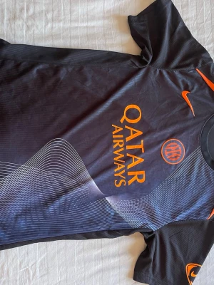 Inter fotbollströja - Köpt utanför san siro. Snygg svart matchtröja från Inter med orangea detaljer och tryck från Qatar Airways. Tröjan har korta ärmar, rund hals och modern grafik framtill. Tillverkad i lätt och ventilerande funktionsmaterial som passar perfekt till fotbollsträning eller match.