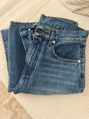 Blå raka jeans från A-DSGN - Säljer ett par klassiska blå jeans från A-DSGN med rak passform och fem fickor. Jeansen har en snygg mellanblå tvätt och detaljer i kontrastsömmar. Perfekta för en avslappnad och stilren look. Materialet är kraftig denim i bomull.