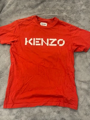 Röd Kenzo t-shirt med logga - Snygg röd t-shirt från Kenzo med stor vit logga framtill. Klassisk passform och rund halsringning. Perfekt för dig som vill ha en enkel men ändå ”fancy” t-shirt.