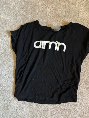 Svart AIM'N t-shirt med tryck - Snygg svart t-shirt från AIM'N med vitt logotryck på bröstet. Klassisk rund hals och korta ärmar. Tillverkad i mjuk bomull som känns skön mot huden. Perfekt för en avslappnad och sportig stil.