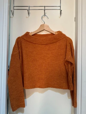 Rostbrun ribbstickad tröja - Säljer en croppad, ribbstickad tröja i en snygg rostbrun färg. Tröjan har bred krage, långa ärmar och är gjord i ett mjukt, tjockt material som känns riktigt cozy. Perfekt till höstlooken och enkel att matcha med jeans eller kjol.