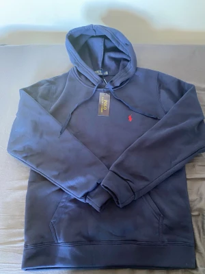 Ralph Lauren hoddie  - Snygg mörkblå hoodie från Polo Ralph Lauren med klassisk röd logga broderad på bröstet. Hoodien har huva med dragsko, magficka och ribbade muddar. Inga skador eller hål 