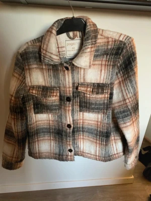 Rutig jacka i ullmix från Pageone - Säljer en snygg rutig jacka från Pageone i beige, svart och rostbrunt. Jackan har två bröstfickor med lock, knappar framtill och klassisk krage. Materialet är mjukt som ger en mysig känsla.