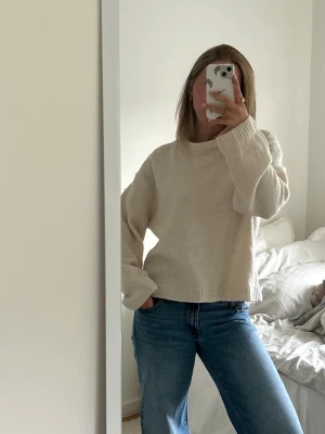 Beige oversized stickad tröja - Säljer en beige oversized stickad tröja med rund hals och långa ärmar. Tröjan har en avslappnad passform och ribbade muddar vid ärmslut och nederkant. Den har lite defekter på ärmarna som möjligtvis går att ta bort