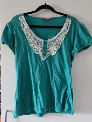 Turkos topp med spetsdetaljer - Säljer en turkos topp med korta ärmar och en bred, vit spetskrage. Perfekt för dig som gillar romantiska detaljer och vill ha något unikt i garderoben.