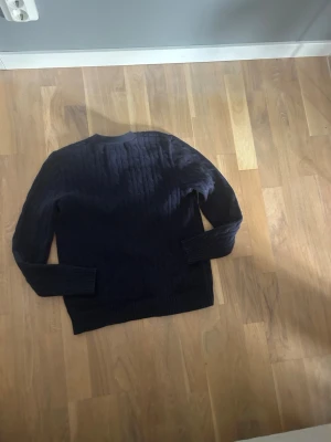 Mörkblå kabelstickad tröja Polo Ralph Lauren - Snygg mörkblå kabelstickad tröja från Polo Ralph Lauren. Tröjan har rund halsringning, långa ärmar och ribbade muddar vid ärmslut och nederkant. Tillverkad i mjukt material som passar perfekt till höst och vinter men även sommarkvällar hör av er vid frågor 