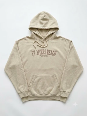 Beige hoodie Ft. Myers Beach - Snygg beige hoodie från U.S. Vintage med trycket 'FT. MYERS BEACH FLORIDA' på bröstet. Klassisk känguruficka framtill, ribbade muddar och justerbar huva. Tillverkad i en mjuk bomulls- och polyestermix som känns skön mot huden.