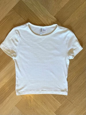 Vit ribbad croppad t-shirt - Fin vit ribbad t-shirt med croppad passform och korta ärmar🥰. Mjukt material och fin passform. Tyvärr för liten för mig och säljer därför