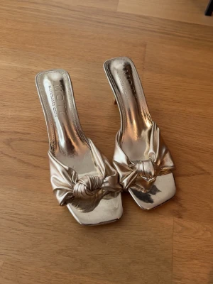 Guldiga pumps med knutdetalj - Säljer ett par glansiga guldiga pumps från Moit med fyrkantig tå och snygg knutdetalj framtill. Skorna har öppen häl och smal klack, perfekta för att lyfta vilken outfit som helst. Materialet är metallic och ger en lyxig känsla. De är från Shein, och nypris är ungefär 260kr🩷Har aldrig använt dom utomhus, endast testade inomhus.