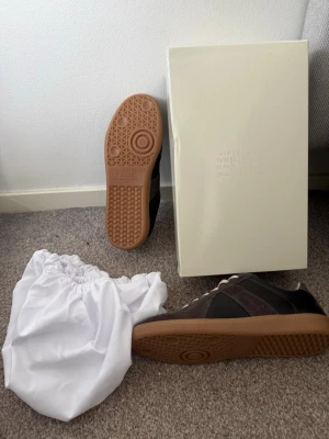 Gats sneakers brun/svart - Gats sneakers i brunt och svart mocka och läder, med beige snörning och klassisk gummisula. Snygg retrostil med låg profil och diskreta detaljer. Kommer med originalkartong och dustbag.