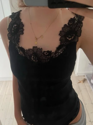 Svart ribbad linnetopp med spets - Säljer en svart ribbad linnetopp med breda axelband och snygga spetsdetaljer runt ringningen. Toppen är figurnära och har en feminin vibe som passar perfekt till jeans eller kjol. Perfekt för dig som vill ha en enkel men ändå extra topp.