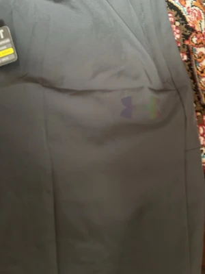 Svarta träningsshorts från Under Armour - Snygga svarta träningsshorts från Under Armour med diskret logga och text i regnbågsfärg på benet. Shortsen har elastisk midja och är tillverkade i ett lätt och snabbtorkande syntetmaterial, perfekta för gymmet eller löprundan.