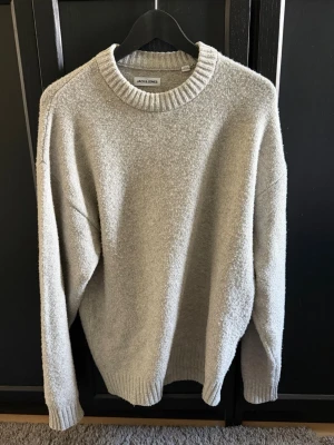 Beige/grå stickad tröja från Jack & Jones - Mysig beige/grå stickad tröja från Jack & Jones med rund halsringning, den är S men sitter som M. Tröjan har en avslappnad passform och är tillverkad i ett mjukt material som passar perfekt för kyligare dagar.