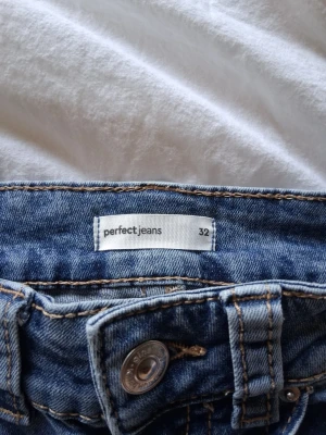Blå slitna bootcut jeans - Säljer ett par blå bootcut jeans från perfect jeans i storlek 32. Jeansen har slitna detaljer och klassisk femficksmodell med knapp och dragkedja. Perfekt för dig som gillar en avslappnad och trendig stil.
