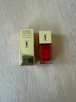YSL La Laque Couture rött nagellack - Lyxigt rött nagellack från Yves Saint Laurent, La Laque Couture. Kommer i en elegant fyrkantig glasflaska med guldfärgat lock och matchande förpackning. Perfekt för dig som vill ha en klassisk och intensiv röd färg på naglarna. Helt oanvänt.