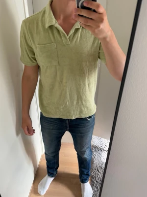 Ljusgrön frottépiké med krage - Säljer en ljusgrön pikétröja i mjuk frotté med klassisk krage och kort ärm. Tröjan har en bröstficka och avslappnad passform, perfekt för en chill och stilren look. 