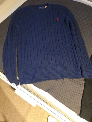 Marinblå kabelstickad tröja Polo Ralph Lauren - Kabelstickad marinblå tröja från Polo Ralph Lauren. Tröjan har rund halsringning, ribbade muddar och nederkant samt ett klassiskt kabelmönster över hela plagget. Perfekt för dig som gillar tidlös och stilren design. Storlek S. Köptes i vintras.