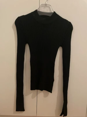 Svart ribbad polotröja Gina Tricot - Säljer en svart, ribbstickad polotröja från Gina Tricot. Tröjan har lång ärm, figurnära passform och hög krage. Perfekt basplagg till garderoben och enkel att styla med olika outfits. Tröjan är glittrig och har slits vid handleden som design 