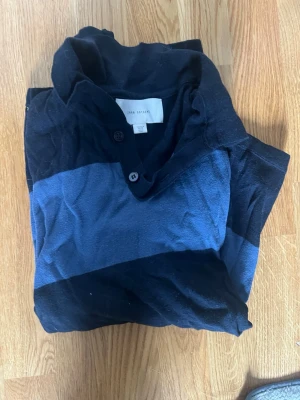 Randig långärmad tröja Zara Man - Snygg långärmad tröja från Zara Man med breda svarta och mörkblå ränder. Tröjan har krage med knappar och är tillverkad i ett mjukt material, perfekt för en avslappnad stil. Säljer då den är lite för kort i längden på mig. Passar dig som gillar klassiska men ändå trendiga plagg.