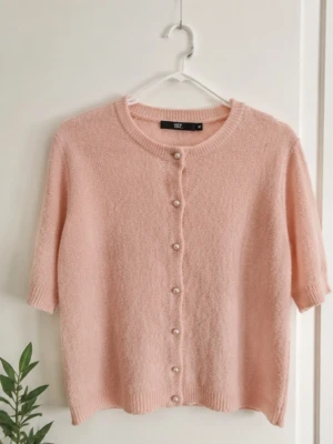 Ljusrosa kofta med pärlknappar - Supersöt ljusrosa kofta med korta ärmar och rund hals. Koftan har fina pärlknappar framtill och är stickad i ett mjukt material. Perfekt att styla över en topp eller klänning för en gullig look.