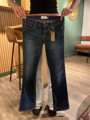 Mörkblå bootcut jeans från Abercrombie  - Säljer ett par mörkblå bootcut jeans från Abercrombie. Jeansen har låg midja, utsvängda ben och detaljerade bakfickor. Perfekta för dig som gillar vintage 2000s style och vill ha ett par jeans som sticker ut.