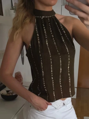 Halterneck topp med mönster från H&M - Säljer en grön halterneck topp med vita vertikala ränder från H&M. Toppen har hög hals och är ärmlös. Perfekt att matcha med jeans eller kjol.