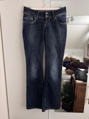 Tommy hilfiger bootcut jeans med låg midja - Kan bara börja med att säga att dessa är sjukt snygga, materialet av jeansen är verkligen den jeansen man vill ha under hösten. Fick jätte fin kroppsfigur i dessa. Endast använda 2 gånger och tyvärr blev de små sen dess. Jag älskar de här jeansen och du kommer också göra det! Dessa passar till långa tjejer också!                                  Innerben: 83-84 cm ungefär Längden i helhet: 109 cm Midja: 37 x 2 cm  Grenhöjd: 16 cm  Bootcut längd: 23 cm  