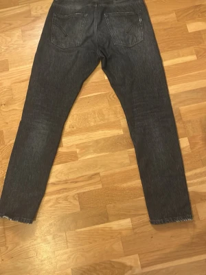 Dondup jeans - Säljer ett par svarta/mörkgrå dondup jeans med fin passform och klassiska fem fickor. Jeansen har slitna detaljer vid bensluten och subtila slitningar framtill. Materialet är denim i bomull och de har en tidlös look som passar till det mesta.
