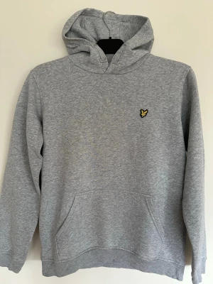 Grå hoodie med broderad logga (Lyle & Scott) - Lyle & Scott hoodie, stl 14/15 år Mycket fint skick. Grå hoodie med broderad örnlogga framtill. Mjuk och skön med fleeceinsida. Inga fläckar eller anmärkningar, mycket gott skick. Tröjans storlek är junior - 14/15 years.