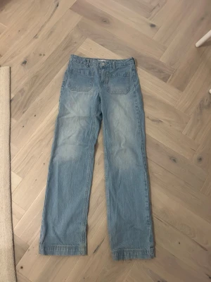 Ljusblå raka jeans med fickor fram - Säljer ett par ljusblå jeans med raka ben och två stora fickor framtill. Jeansen har även klassiska bakfickor och är tillverkade i denim. Perfekta för en avslappnad och trendig look.