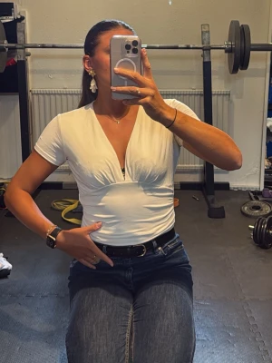 Vit v-ringad topp med kort ärm - Säljer en vit topp med v-ringning och korta ärmar. Toppen har en figurnära passform och markerad midja som ger en snygg siluett. Perfekt att matcha med jeans eller kjol för en clean och fräsch look.