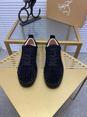 Louboutins  - Säljer ett par svarta sneakers från Christian Louboutin i mocka med svarta nitar på tån. Skorna har svarta skosnören, låg profil och klassisk röd sula. Perfekta för dig som vill sticka ut med en edgy och lyxig stil.