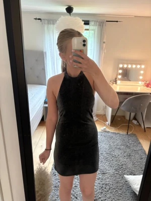 Svart glittrig kort klänning - Säljer en svart glittrig kort klänning med halterneck och ärmlös design. Klänningen har en tight passform och skimrande material som fångar ljuset snyggt. Perfekt för dig som vill sticka ut med en enkel men ändå festlig look. Klänningen är från Cubus i storlek 152. Fler bilder kan skickas, vid visat intresse😊