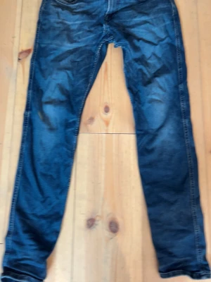 Mörkblå slim fit jeans herr från replay - Snygga mörkblå jeans i slim fit-modell med klassisk femficksdesign och lätt slitna detaljer. Jeansen har normal midja och raka ben, perfekta för en avslappnad och trendig look.